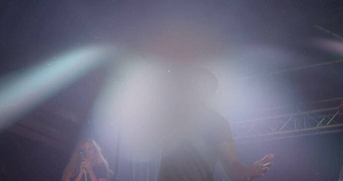 Lead singer singing wired mic, backing singer raising tambourine as lights flaring during music set