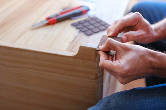 Hands applying furniture glider pads to wood