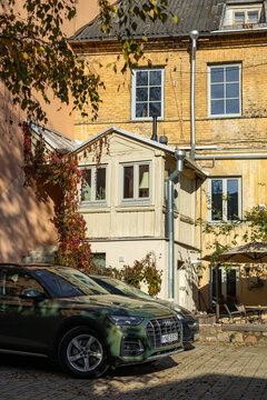 Vilnius, Lithuania - October 21 2025: Vilnius courtyard scene with parked Audi Q5 SUV in front of historic residential building, yellow brick facade and wooden balcony extension. Warm autumn sunlight