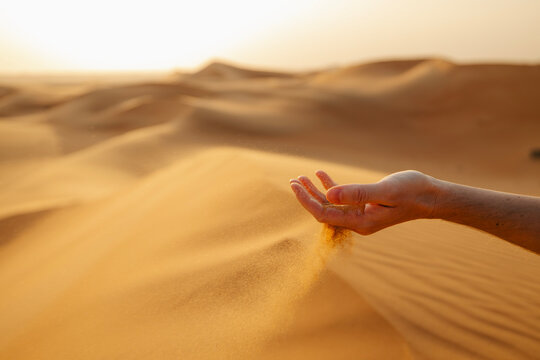 Close-up of hand letting sand flow in wind in Abu Dhabi desert, UAE. Desert textures, natural elements, travel, adventure, and Middle East landscape concept.