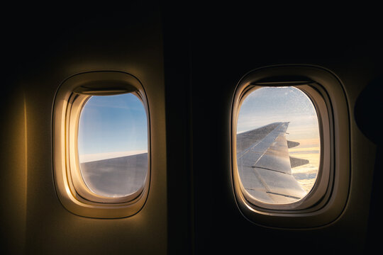View through airplane window showing aircraft wing illuminated by early sunrise light during flight. Travel atmosphere, aviation journey, peaceful morning sky, and passenger perspective concept.