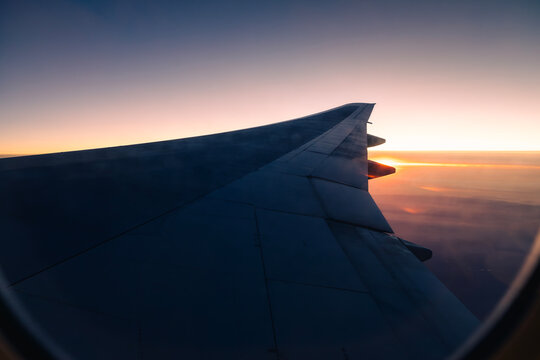 View through airplane window showing aircraft wing illuminated by early sunrise light during flight. Travel atmosphere, aviation journey, peaceful morning sky, and passenger perspective concept.