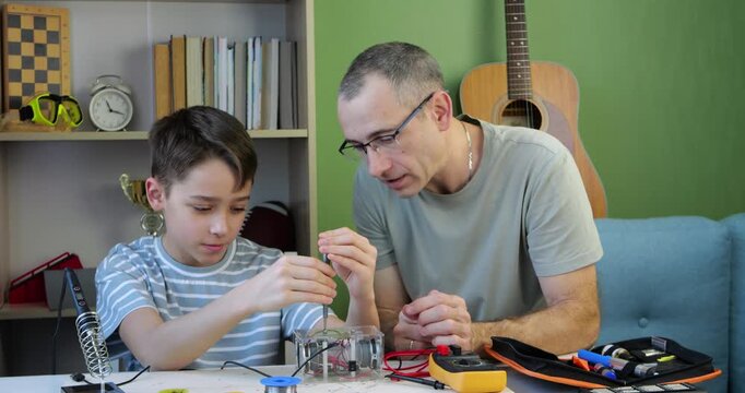 Father teaches son electronics concepts. Dad and child explore circuits together at home. Engaging learning experience strengthens bond. This educational moment encourages creativity and curiosity.