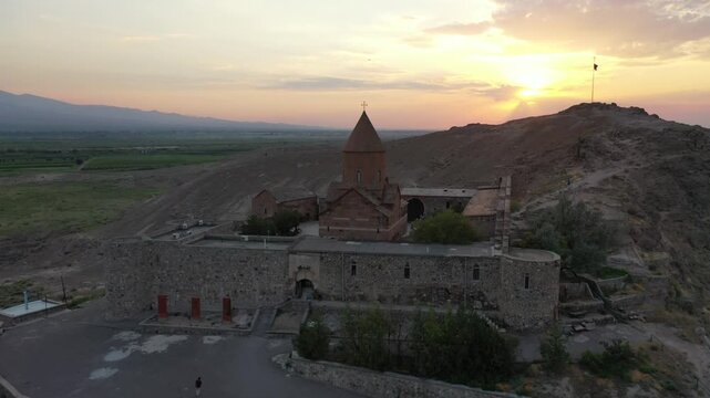 Aerial drone footage flying over the ancient Khor Virap monastery in Armenia. The historic stone complex sits on a hill with the magnificent Mountain in the background.

