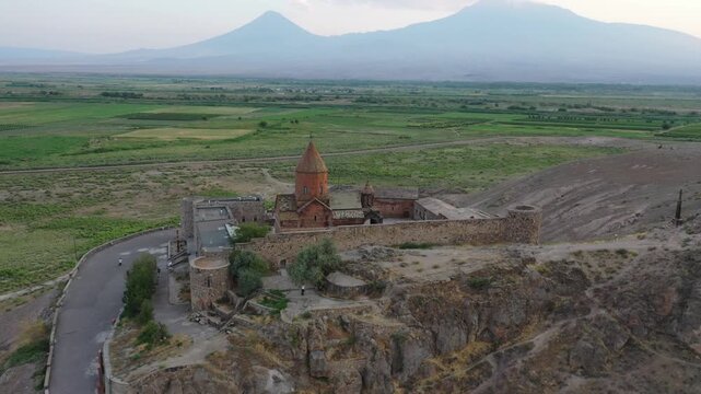 Aerial drone footage flying over the ancient Khor Virap monastery in Armenia. The historic stone complex sits on a hill with the magnificent Mountain in the background.


