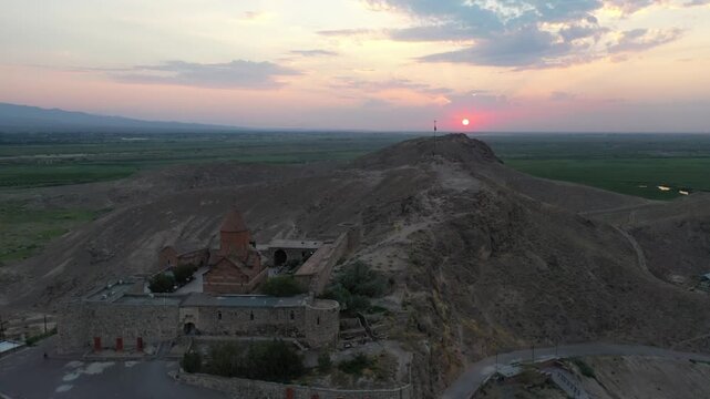 Aerial drone footage flying over the ancient Khor Virap monastery in Armenia. The historic stone complex sits on a hill with the magnificent Mountain in the background.

