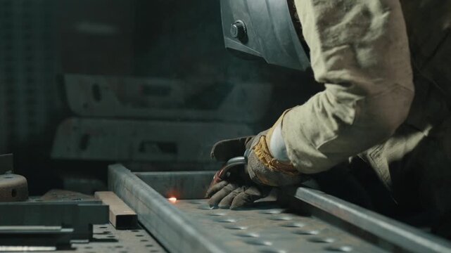 Welder in protective clothing welds metal parts in the workshop. Slow motion.