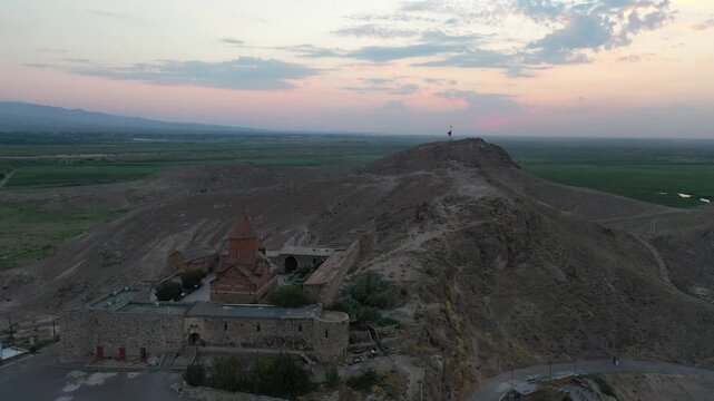 Aerial drone footage flying over the ancient Khor Virap monastery in Armenia. The historic stone complex sits on a hill with the magnificent Mountain in the background.


