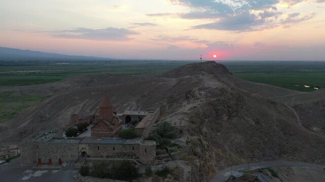 Aerial drone footage flying over the ancient Khor Virap monastery in Armenia. The historic stone complex sits on a hill with the magnificent Mountain in the background.

