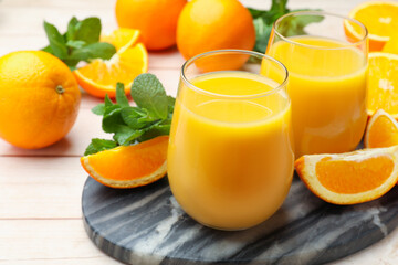 Citrus juice in glasses, fresh oranges and mint leaves on light wooden table, closeup © New Africa