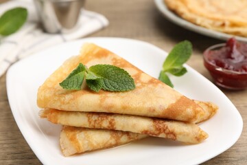 Tasty crepes with mint leaves and jam served on wooden table, closeup © New Africa