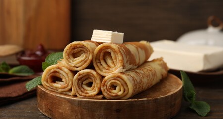 Tasty rolled crepes with butter and mint leaves served on wooden table, closeup © New Africa