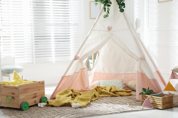 Toy wigwam with pillows, wooden cart, furniture and floral decor in room © New Africa