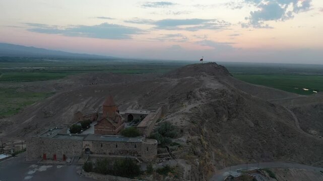 Aerial drone footage flying over the ancient Khor Virap monastery in Armenia. The historic stone complex sits on a hill with the magnificent Mountain in the background.

