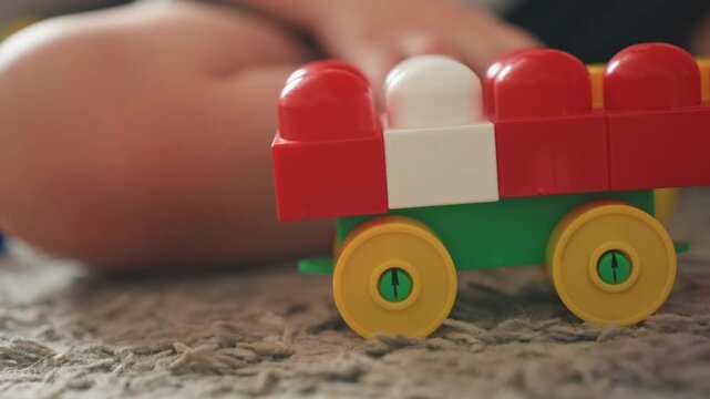 White boy hands pushing toy train on carpet, closeup of yellow wheels rolling and red plastic blocks, tactile play and fine motor practice, cozy indoor floor scene with warm natural light and playful