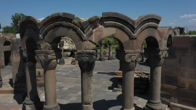 Aerial drone footage reveals the spectacular ancient stone ruins of Zvartnots Cathedral in Armenia. The top-down perspective highlights circular columns, intricate foundations, and tourists exploring 
