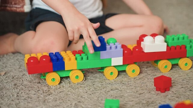 White son building colorful block train on carpet, focused hands placing large plastic bricks, vibrant train with wheels, cozy indoor playtime, creative learning and fine motor development, joyful