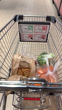 Shopping cart with groceries moving in supermarket aisle close up view inside trolley