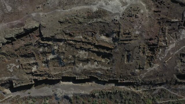 Aerial drone footage offering an overhead view of ancient stone ruins. The archaeological site features complex foundations of a historic settlement in a dry, rocky, arid natural landscape.

