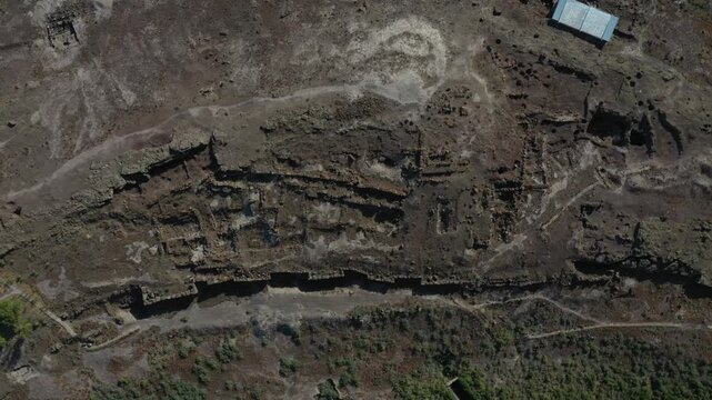 Aerial drone footage offering an overhead view of ancient stone ruins. The archaeological site features complex foundations of a historic settlement in a dry, rocky, arid natural landscape.

