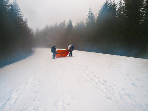 Two young men drag a tent along a snowy road in the wilderness