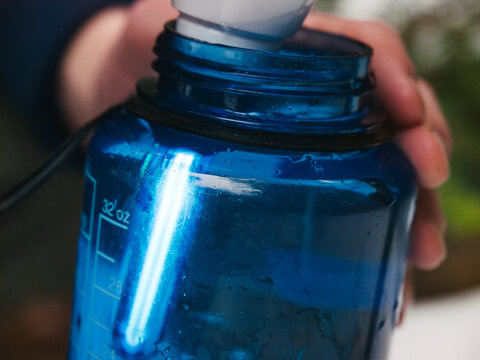 A young man filters water from a stream into a water bottle using a ultraviolet-light filter while backpacking in winter.