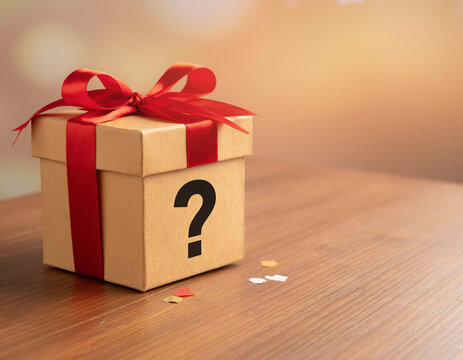 A cardboard gift box with a red ribbon and a question mark symbol on a wooden table, embodying the concept of mystery, surprise, promotion, and a secret offer.