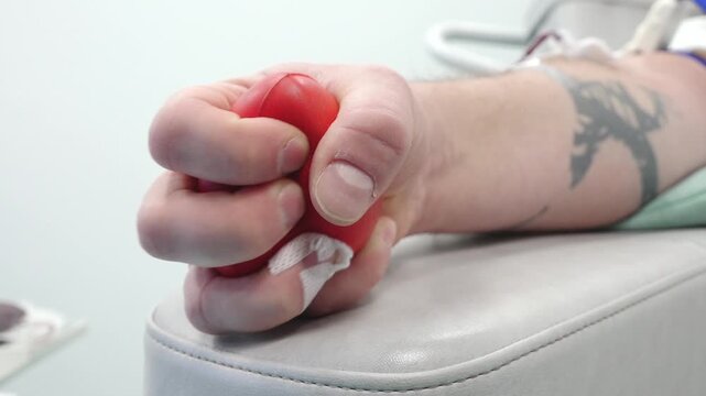Person donating blood grips a red stress ball tightly while seated in a medical facility, showcasing the donation process in action