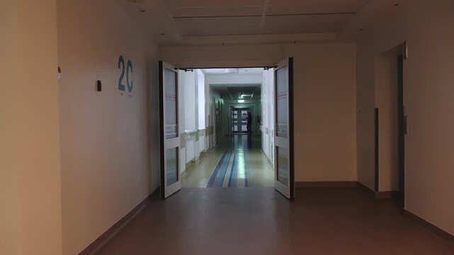 Hospital corridor with open doors leading to room 2C, showing a continuous view of the hallway and approaching figure in scrubs