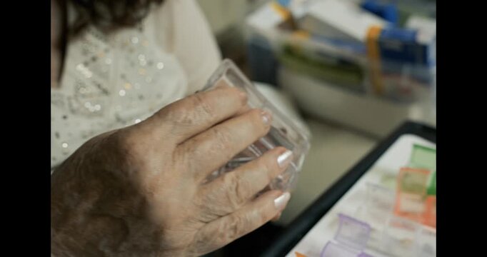 Senior woman using a pill splitter to cut medication in half while sitting at home. Concept of healthcare routine, dosage control and medication management for elderly people.