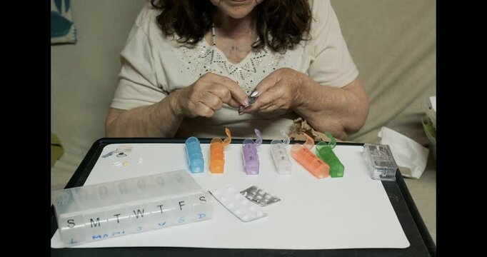 Older adult woman organizing prescription pills into a weekly pill organizer in her living room. Concept of healthcare routine, aging and independent senior lifestyle.