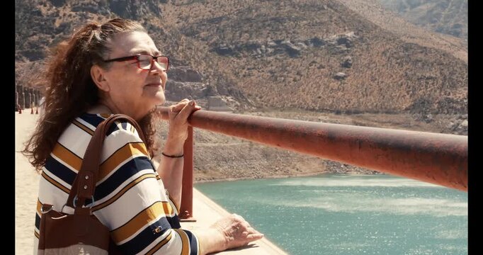 Senior woman standing and looking at a lake while enjoying a peaceful vacation. Concept of retirement freedom, active aging and independence while traveling.
