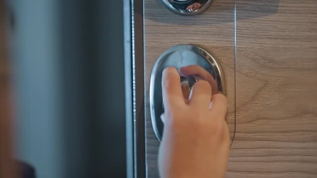 Young caucasian son turning doorknob indoors, blue coat and knit hat, closeup on small hands and face showing curiosity and slight anxiety as he struggles to open locked entrance while caring mom