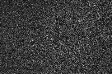 Fototapeta premium Top view of black asphalt road texture. Dark granular bitumen surface close-up for road construction and transport background. Gritty stone pavement pattern.