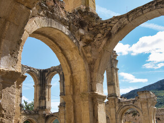 Obraz premium Long perspective view of ancient stone archways and cloisters - Architectural ruins of a historic monastery or abbey with sunlight streaming through the open arches and blue sky above.