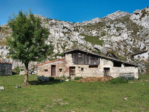 Rustic stone mountain hut ('majada') with a wooden upper level and tiled roof - Traditional rural building set against a rugged, rocky limestone mountainside under a blue sky.
