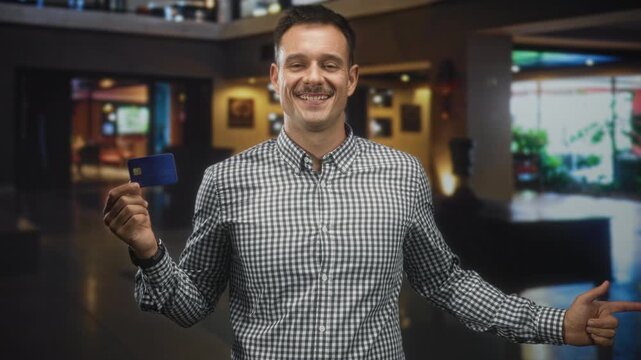 Man with moustache holding a blue creditcard in left hand and pointing right finger inside a building;confidence trust.