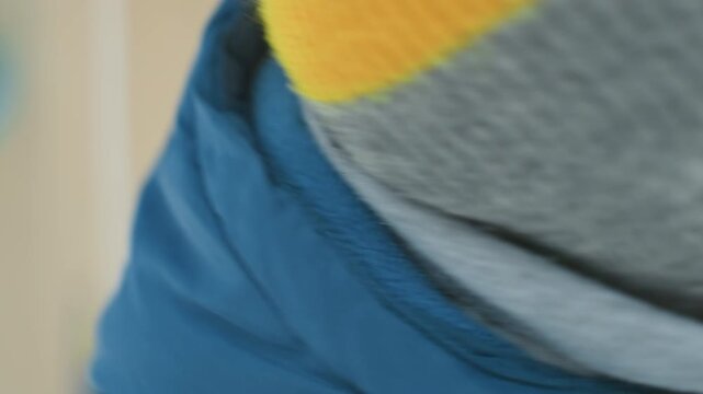 Closeup caucasian toddler blowing icy bubble outdoors wearing blue jacket and grey beanie, pursed lips releasing frozen soap film, mittens visible, soft winter light, gentle playful mood