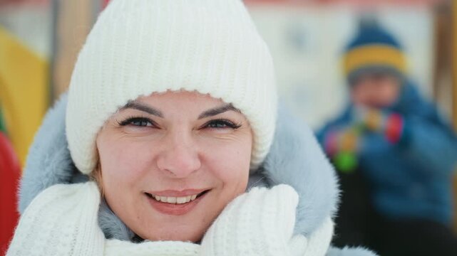 Mom and son playful snowball at playground candid reaction sequence, woman in white knit hat and scarf reacting from surprise to smile, blurred child tossing snow in colorful outdoor playset, dynamic