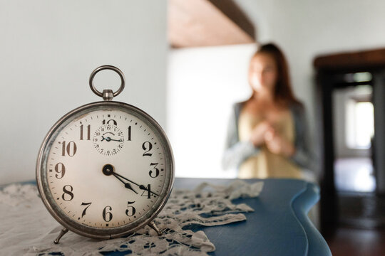 Vintage clock in foreground with young woman by window in background