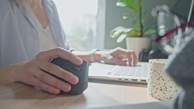 Woman clicking computer mouse and scrolling wheel at desk with laptop in home workspace. Concept of computer use and navigation