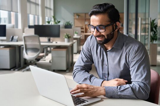 Hispanic indian smiling businessman wearing glasses and headset having virtual team meeting call, talking, remotely working at home watching online learning training webinar in remote office.