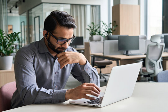 Latin indian serious businessman wearing glasses and headset having virtual team meeting call, remotely working at home watching online learning training webinar in remote office.