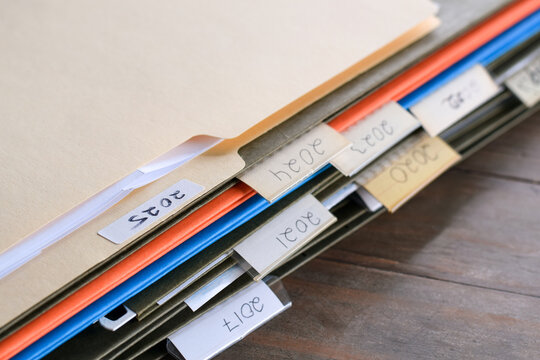 Closeup stack of file folders with past year numbers written on tabs. Organized document storage highlighting archiving, record keeping, and chronological filing system