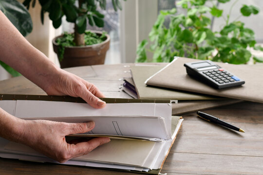 Woman hands searching through file folder on table in home setting. Documents and paperwork visible, highlighting organization, record keeping, and everyday administrative tasks.
