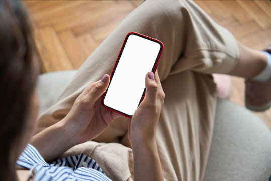 Young woman or teen girl hands holding mobile smart phone with mockup white blank display, empty screen at home. Shopping, delivery apps, social media applications ads, over shoulder close up view.