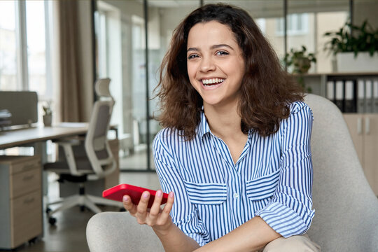 Happy hispanic young woman laughing holding smartphone, portrait. Smiling latin teen girl student having fun enjoying using modern mobile apps on cell phone tech sitting in chair looking at camera.
