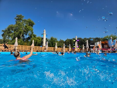 Group of people are swimming in a pool. The water is blue and the sky is clear