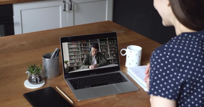 Positive student girl talking to college mate guy on video call, chatting to university friend on laptop, discussing homework, study educational process. Over shoulder view at screen