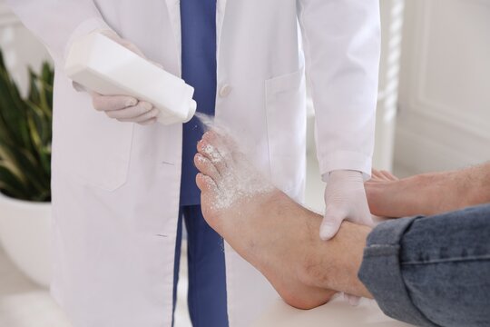 Doctor applying talcum powder onto man's foot in clinic, closeup